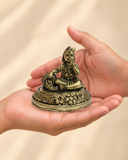 Illustrative scale view of Bal Krishna Brass Idol With Butter Pot resting on an adult open palm; listed height 3.25 inches.