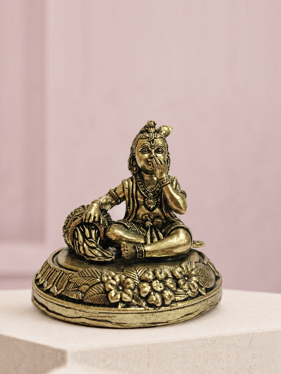 Bal Krishna Brass Idol with Butter Pot on an ivory platform with a soft mauve heritage backdrop