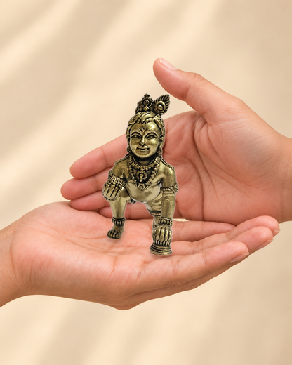 Illustrative scale view of Crawling Bal Krishna Brass Idol resting on an adult open palm; listed height 3.5 inches.