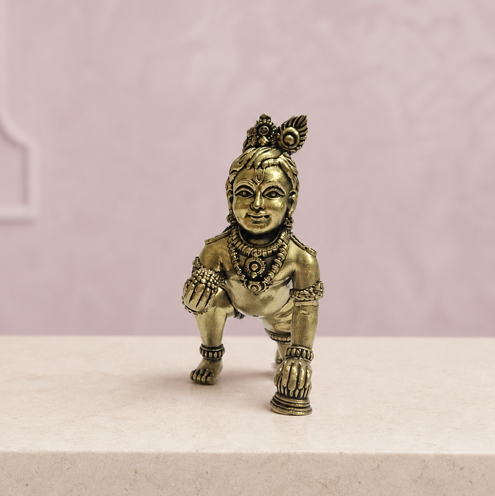 Crawling Bal Krishna Brass Idol on an ivory platform with a soft mauve heritage backdrop