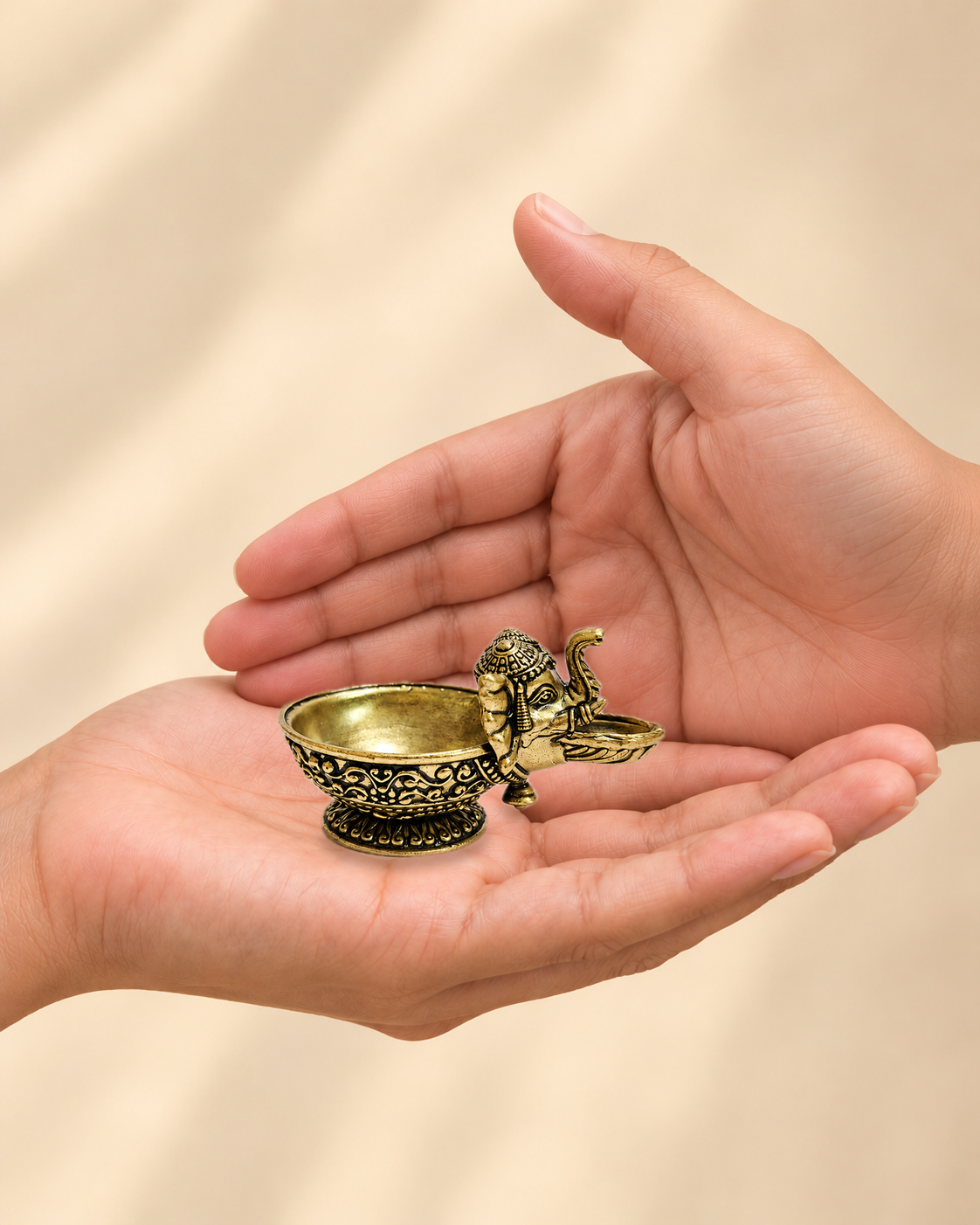 Illustrative scale view of Ganesha Brass Diya Bowl resting on an adult open palm; listed height 1.5 inches.