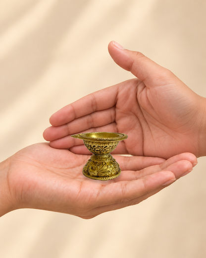 Illustrative scale view of Mini Pedestal Brass Diya resting on an adult open palm; listed height 1.5 inches.