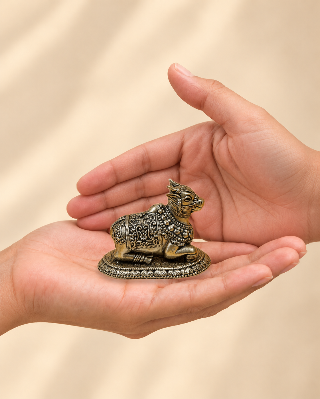 Illustrative scale view of Nandi Brass Idol resting on an adult open palm; listed height 2 inches.