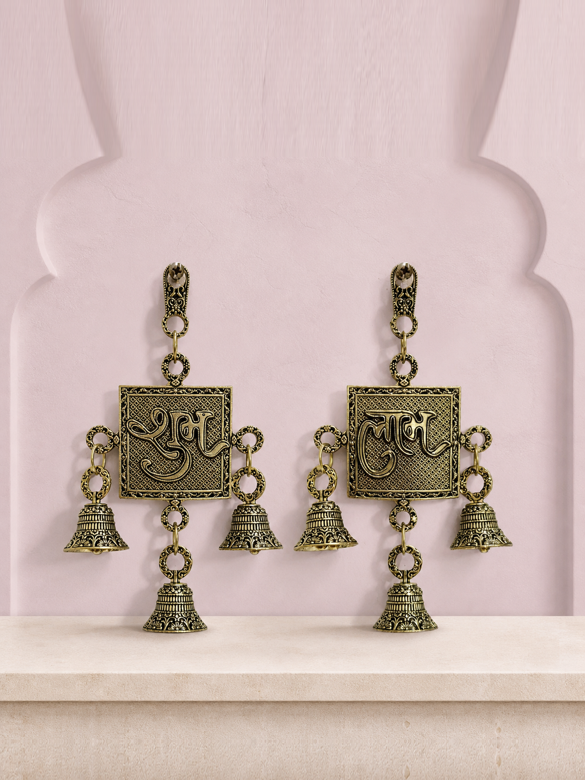 Shubh and Labh brass wall bell set displayed together on a soft mauve heritage wall
